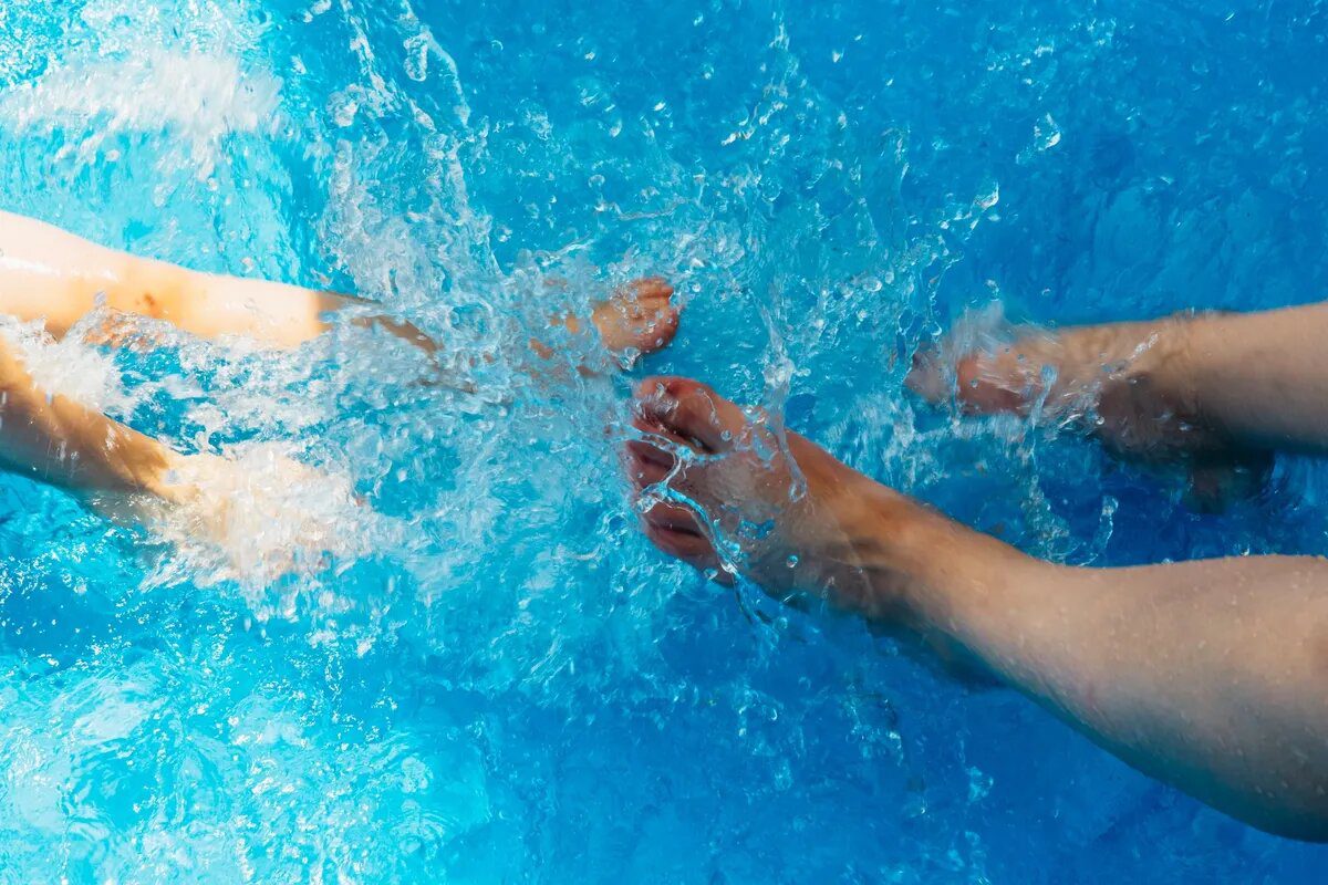 Two people in a pool with their hands touching water.