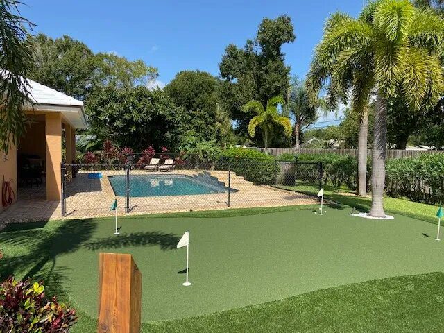 A backyard with a pool and grass golf course.